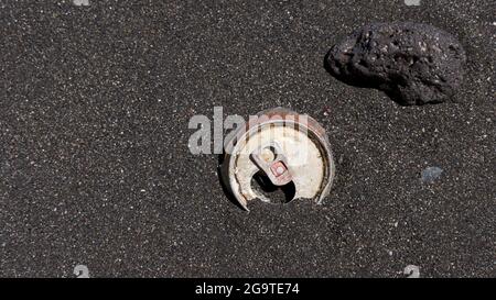 Ausrangierte Getränkebehälter aus Aluminium für Getränkekonserven, die an einem dunklen, sandigen Strand als Teil der großen Müllmasse Anzeichen von Erosion und Verfall aufweisen Stockfoto