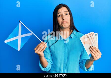 Junge lateinerin mit schottischer Flagge und zerstoßen Banknoten deprimiert und sorgen sich um Not, weinen wütend und ängstlich. Trauriger Ausdruck. Stockfoto