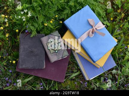 Stillleben mit alten geschmückten Büchern, die draußen auf dem grünen Rasen liegen. Vintage romantisches und pädagogisches Konzept Stockfoto