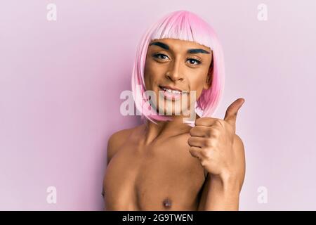 Hispanische Transgender Mann trägt Make-up und rosa Perücke lächelnd glücklich und positiv, Daumen nach oben tun ausgezeichnet und Zustimmung Zeichen Stockfoto