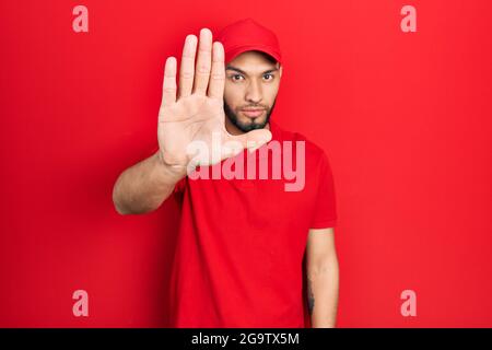 Hispanic Mann mit Bart tragen Lieferung Uniform und Kappe tun aufhören zu singen mit Handfläche der Hand. Warnung Ausdruck mit negativen und ernsten Geste o Stockfoto