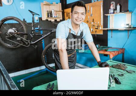 Fahrradmechaniker im Vorfeld, der lächelnde Handschuhe trägt, während er in der Nähe des Laptops steht Stockfoto