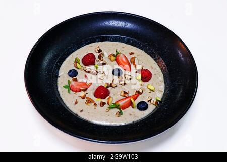 Haferbrei mit frischen gemischten Beeren und trockenen Nüssen in einer Schüssel Stockfoto