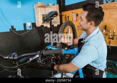 Schöner Fahrradmechaniker in einer Schürze, der Handschuhe trägt, wenn er einen Sattel installiert Stockfoto
