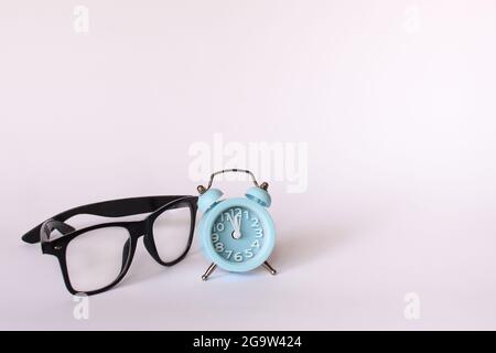 Schwarze Gläser und ein blauer Wecker zeigen 12 zwölf Uhr Stockfoto