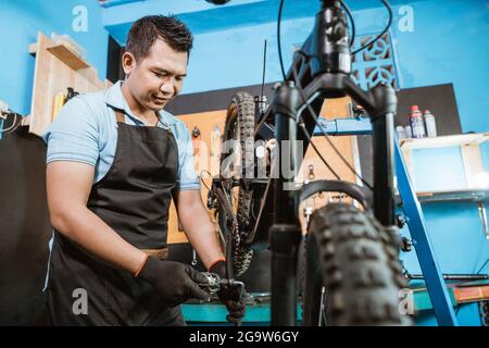Hübscher Fahrradmechaniker in einer Schürze, der Handschuhe trägt, wenn er Fahrradpedale installiert Stockfoto