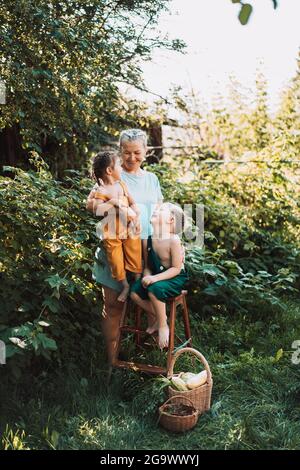 Großmutter mit zwei Enkelkindern, die im Garten stehen und sich gegenseitig glückliche Familie schauen. Stockfoto