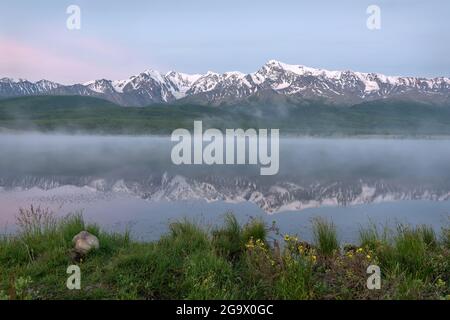 Erstaunlich zarte Sonnenaufgang über den Bergen mit Schnee und Wald bedeckt, Nebel über dem See und schöne Reflexionen im Wasser gegen das blaue sk Stockfoto
