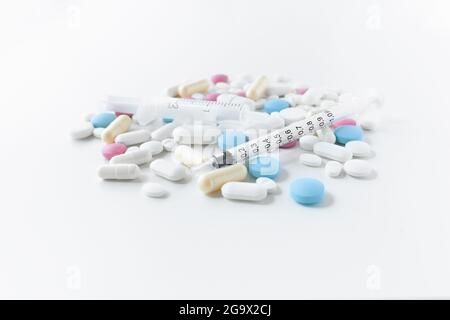 Stapel von blauen, weißen, rosa und gelben Pillen und Kapseln mit medizinischer Spritze mit schwarzen Markierungen auf weißem Hintergrund Stockfoto