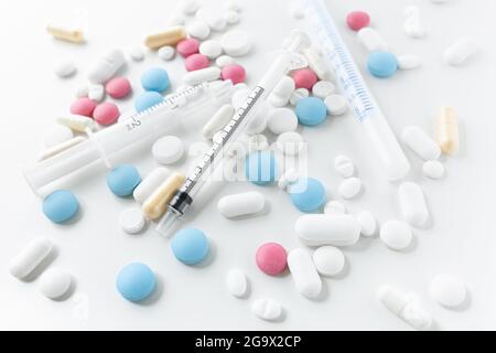 Stapel von blauen, weißen, rosa und gelben Pillen und Kapseln mit medizinischen Spritzen mit schwarzen und blauen Markierungen auf weißem Hintergrund Stockfoto