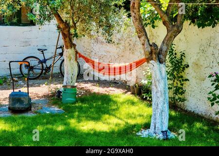 Orangefarbene Hängematte hing zwischen den Bäumen im Garten eines Hauses Stockfoto
