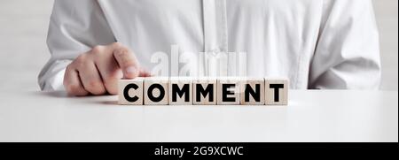 Geschäftsmann drückt mit dem Finger auf die Holzwürfel mit dem Wort Kommentar. Kundenfeedback, Review- oder Meinungskonzept. Stockfoto