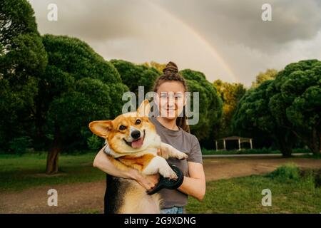 Junge glückliche Frau mit Dreadlocks, die einen kleinen Hundecorgi halten. Stockfoto
