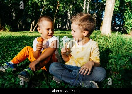 Zwei fröhliche Jungen essen Eis auf Gras im öffentlichen Park. Stockfoto