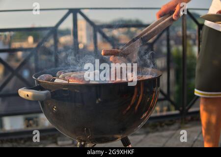 Männliche Hand trägt eine kurze mit einer Zange, um eine Wurst aus tiefen Topf an einem sonnigen Tag abholen Stockfoto