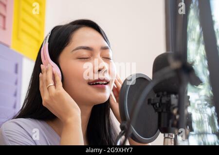 Eine asiatische Sängerin, die beim Singen Kopfhörer trägt und hält Stockfoto