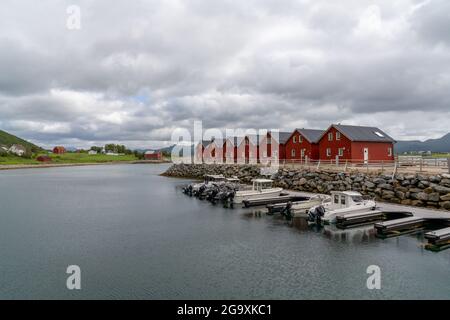 Skreda, Norwegen - 20. Juli 2021: Farbenfrohe rote Holzhäuser am Meer auf den Lofoten-Inseln Norwegens mit Booten am Dock in der Vorgruppe Stockfoto