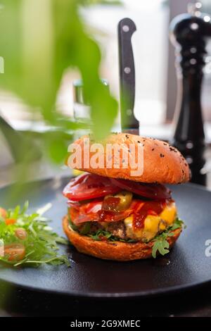 Burger mit Rindfleisch und Gemüse, Gemüsesalat. Fast Food. Der Koch kocht und serviert ein appetitliches Gericht. Das fertige Gericht wurde auf einem Teller serviert. Servin Stockfoto