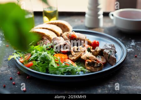 Lebereintopf mit Pilzen und Kirschtomaten, serviert mit Brot und frischem Salat. Der Koch kocht und serviert ein appetitliches Gericht. Das fertige Gericht serviert Stockfoto