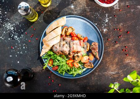 Lebereintopf mit Pilzen und Kirschtomaten, serviert mit Brot und frischem Salat. Der Koch kocht und serviert ein appetitliches Gericht. Das fertige Gericht serviert Stockfoto