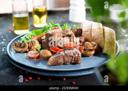 Lebereintopf mit Pilzen und Kirschtomaten, serviert mit Brot und frischem Salat. Der Koch kocht und serviert ein appetitliches Gericht. Das fertige Gericht serviert Stockfoto