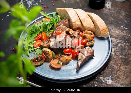 Lebereintopf mit Pilzen und Kirschtomaten, serviert mit Brot und frischem Salat. Der Koch kocht und serviert ein appetitliches Gericht. Das fertige Gericht serviert Stockfoto