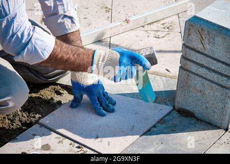 Hände eines türkischen Straßenbauers, der Fliesen mit einem Gummihammer einbaute. Stockfoto