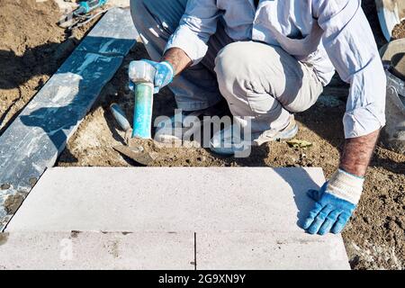 Hände eines türkischen Straßenbauers, der Fliesen mit einem Gummihammer einbaute. Stockfoto