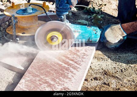 Hände eines Straßenbauarbeiters, der einen Winkelschleifer zum Schneiden der Fliesen verwendet. Stockfoto