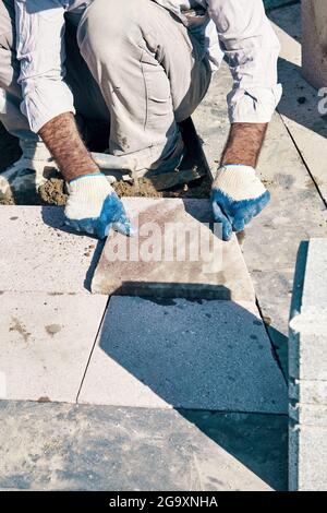 Hände eines türkischen Straßenbauers, der Fliesen installiert und einen Bürgersteig baut. Stockfoto