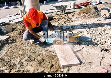 Pflaster-Bauarbeiter mit einem Winkelschleifer zum Schneiden der Fliesen. Stockfoto