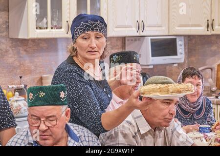 Die Bewohner des sibirischen Dorfes feiern den muslimischen Feiertag Kurban Bayram an ihrem Heimattisch. Frau, die Gästen Honigkuchen anbietet. Eid al-Adha Stockfoto