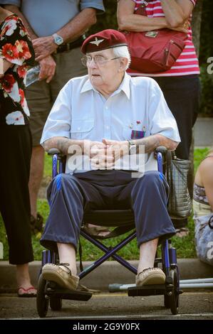 Ein einzelner männlicher Kriegsveteran oder "Zigarren", der auf einem Rollstuhl sitzt und die Parade des ANZAC Day auf der Cairns Esplanade Cenotaph in QLD, Australien, beobachtet Stockfoto