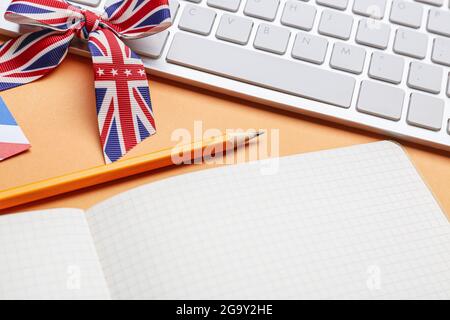 Schreibwaren, Tastatur und Band in den Farben der britischen Flagge auf orangefarbenem Hintergrund. Konzept des Englischlernens Stockfoto