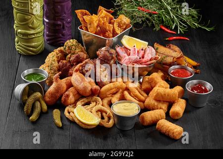 Bier-Snacks mit Saucen, Gurken auf schwarzem Tisch mit Tiki-Statuen Stockfoto