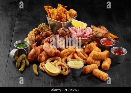 Set herzhafter Biersnacks auf schwarzem Holztisch mit Gewürzen Stockfoto