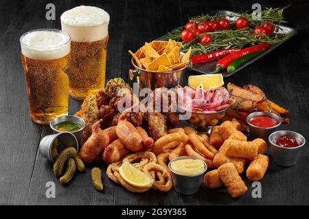 Zwei Gläser Bier mit herzhaften Snacks und Gemüse auf Schwarz Stockfoto