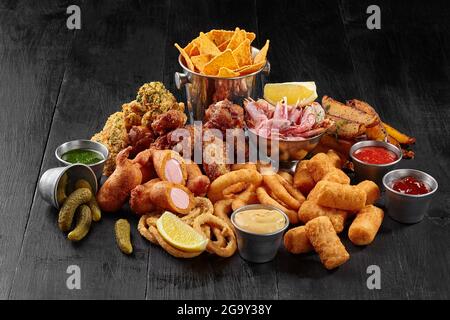 Gebratene Hähnchenflügel, zerschlagene Würste, Zwiebelringe, Käsestäbe, Kartoffelkeile, Maischips und Garnelen Stockfoto