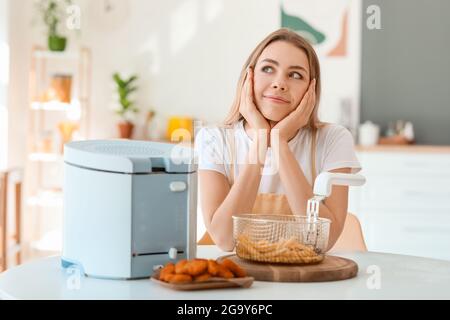 Junge Frau mit Fritteuse und Snacks in der Küche Stockfoto