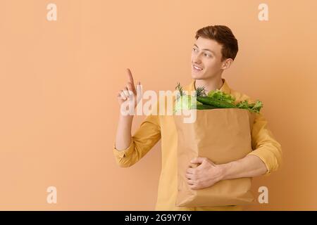 Junger Mann mit Papiertüte und frischem Gemüse auf farbigem Hintergrund Stockfoto