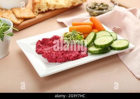 Teller mit leckerem Rübenhummus, Karotten und Gurken auf farbigem Hintergrund Stockfoto