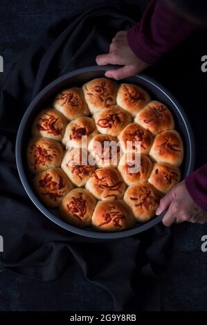 Blick von oben auf eine Person, die ein mit frisch gebackenen Brötchen gefülltes Backblech hält Stockfoto