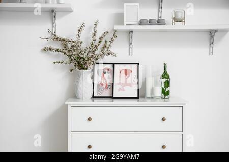 Vase mit schönen blühenden Ästen auf Kommode im Zimmer Stockfoto