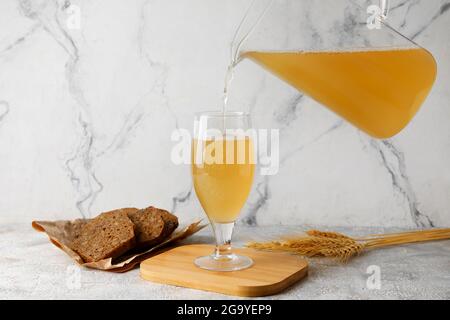 Gießen von frischem Kvass in Glas auf hellem Hintergrund Stockfoto
