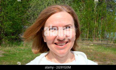 Schöne reife Frau Gesicht. Dame mit mittlerem Erwachsenenalter, die im Freien lächelt. Porträt einer Frau im Alter von 55-60 Jahren beim Entspannen im Garten. Stockfoto