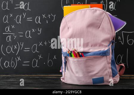 Schulrucksack mit Schreibwaren auf Tisch neben Tafel Stockfoto