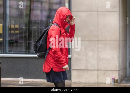 Frau in rotem Anorak mit Kapuze in Preston, Lancashire. UK Wetter 28. Juli 2021; Morgenregen im Stadtzentrum mit weiteren starken Schauern erwartet. Credit MediaWorldImages/AlamyLiveNews. Stockfoto