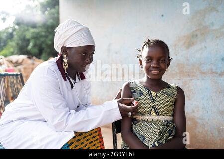 In diesem Bild lacht ein schönes afrikanisches Mädchen mit witzigem Haistyle direkt in die Kamera, die neben einem sanft lächelnden Nurs sitzt, das ihr T misst Stockfoto