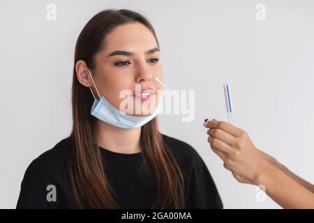 Arzt, der einen nasalen PCR-Test mit Covid-19 für junge weibliche Patienten über hellem Studiobild vorstellt Stockfoto