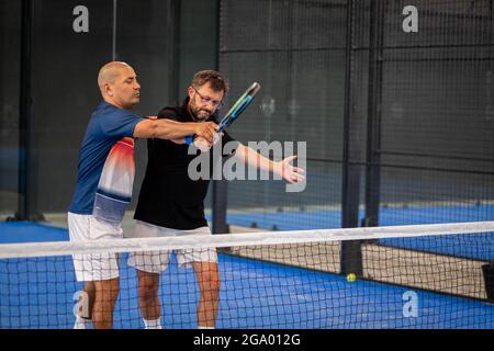 Überwachen Sie den Padel-Unterricht für den Mann, sein Schüler - Trainer lehrt Jungen, wie Padel auf dem Hallentennisplatz zu spielen Stockfoto